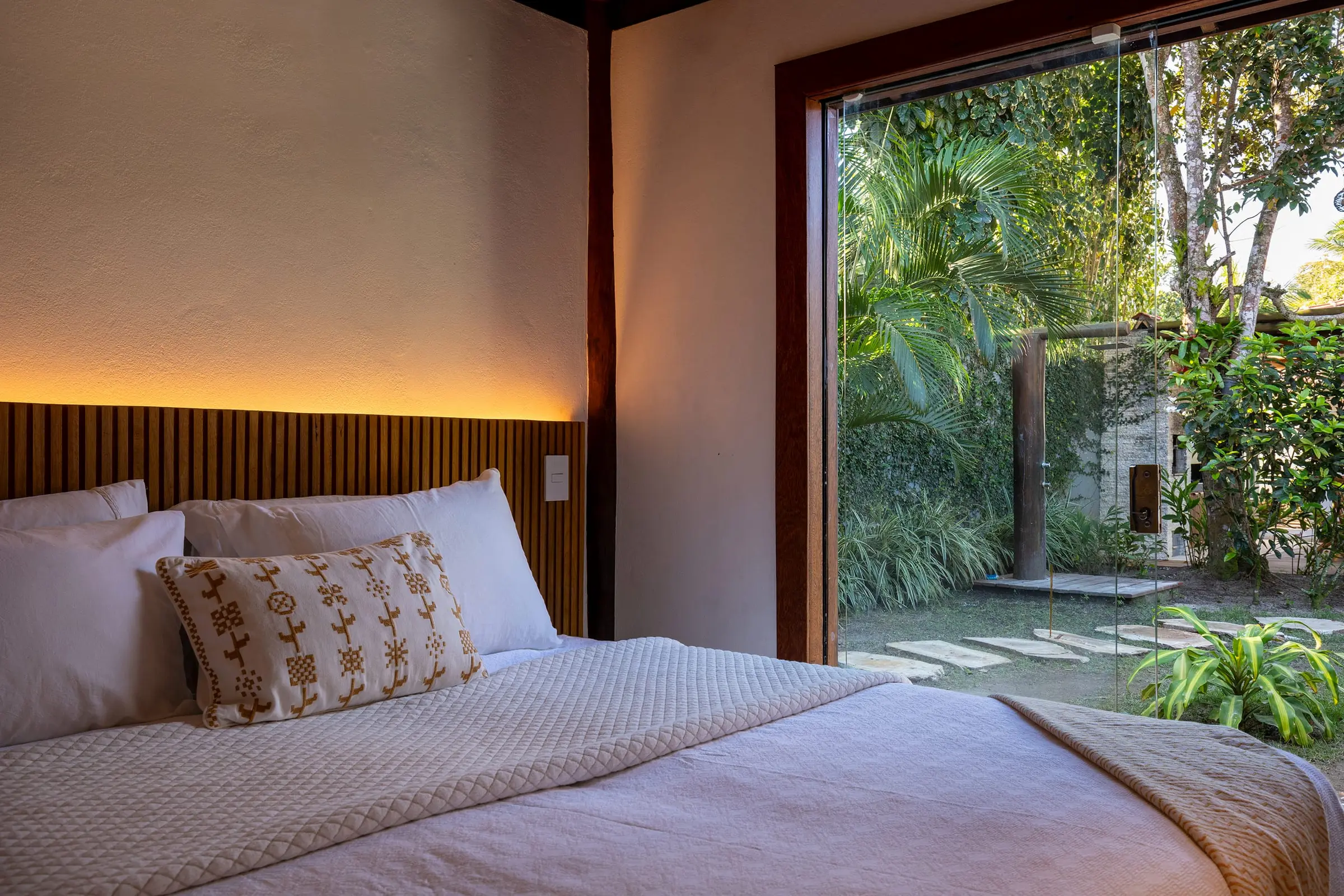 Quarto com cabeceira estofada e vista para o jardim
