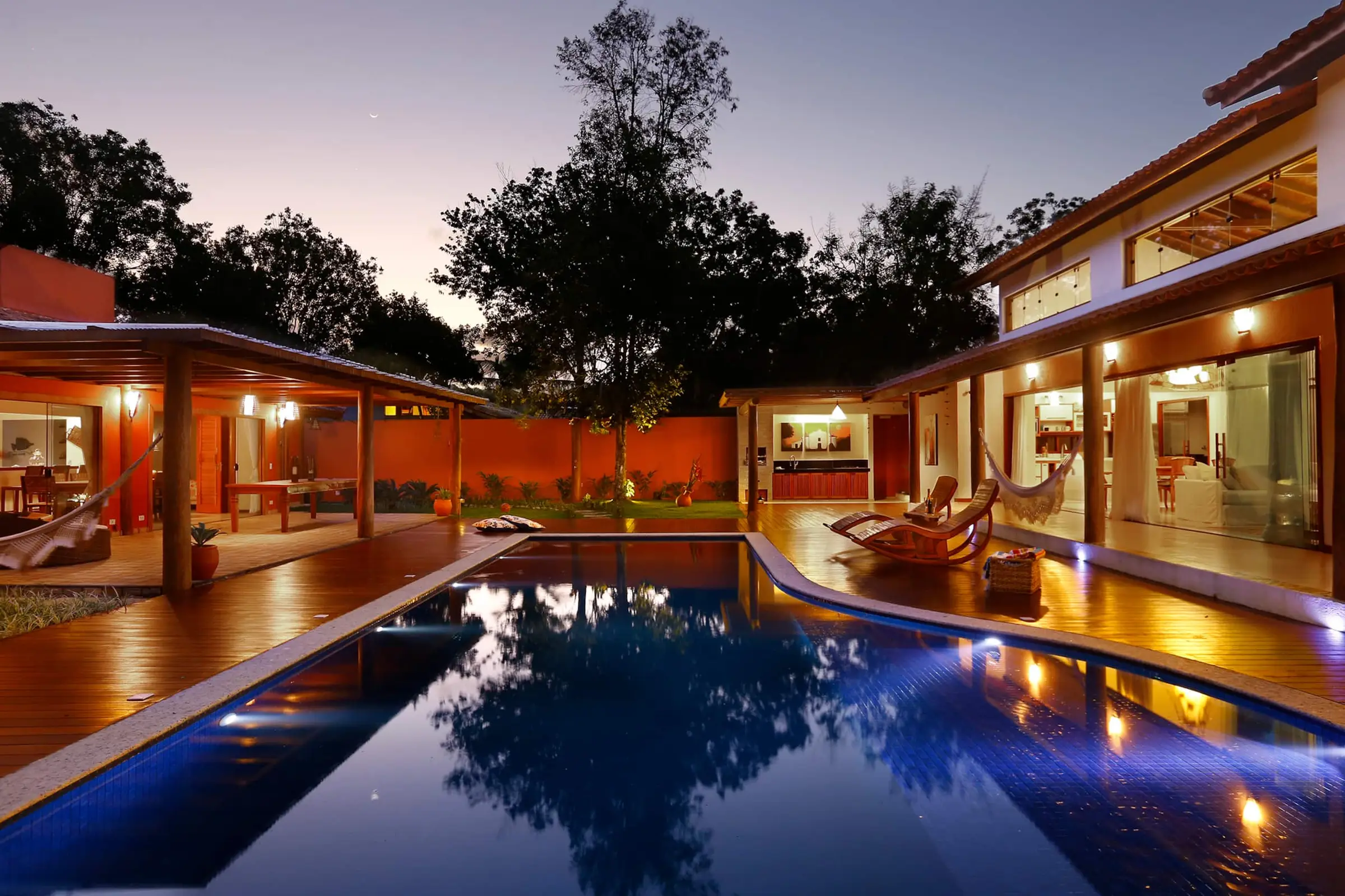 Vista noturna da piscina entre as duas casas da Natura Paradise, com as fachadas iluminadas ao entardecer