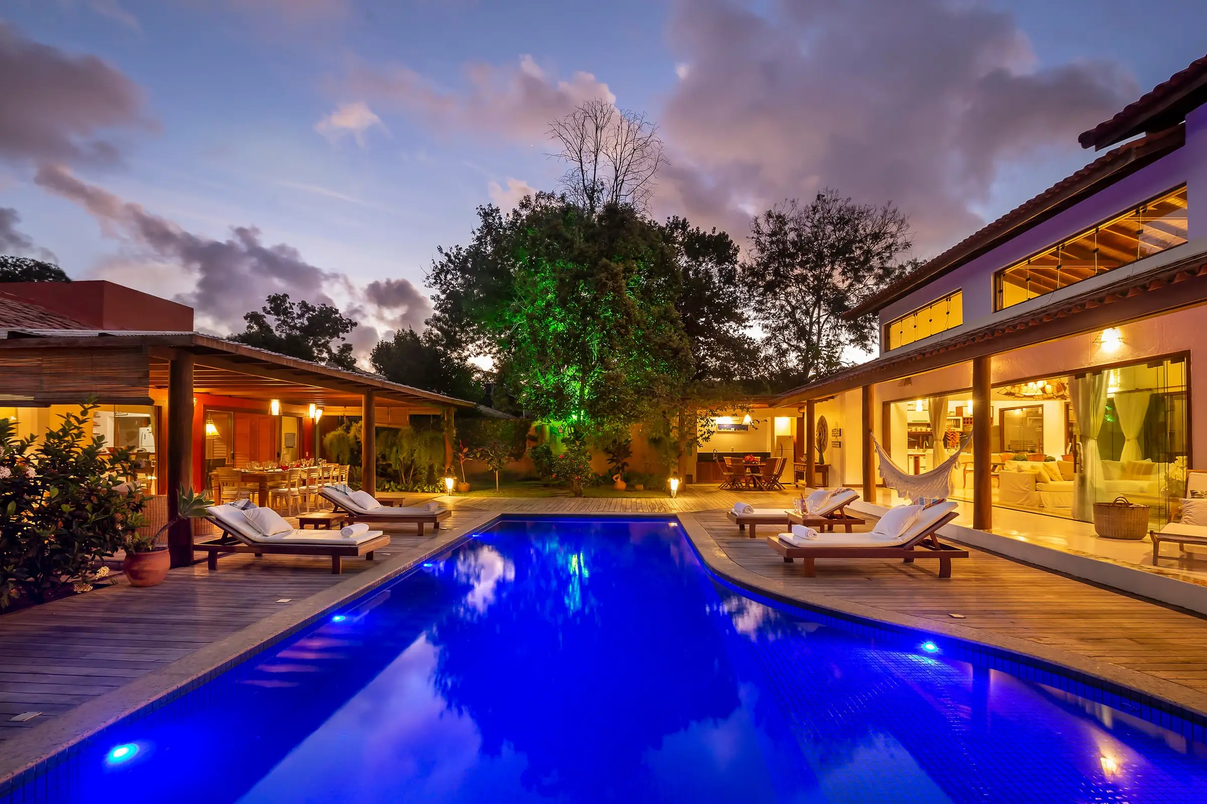 Piscina iluminada ao entardecer, ladeada pelas duas casas da vila